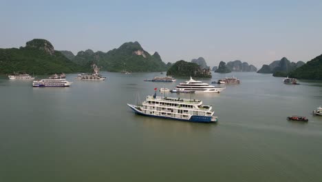 aerial of traditional white cruise ship traveling through waters of ha long bay vietnam around limestone mountains at sunrise