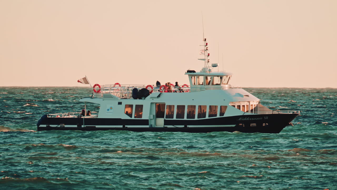 Cannes, France - November 18, 2025: A side view of a passenger ferry named Mediterranee XII, sailing over wavy waters under warm sunset light