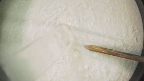 pouring water into preparation tank with white milk and curd at cheese factory, close up, slow motion