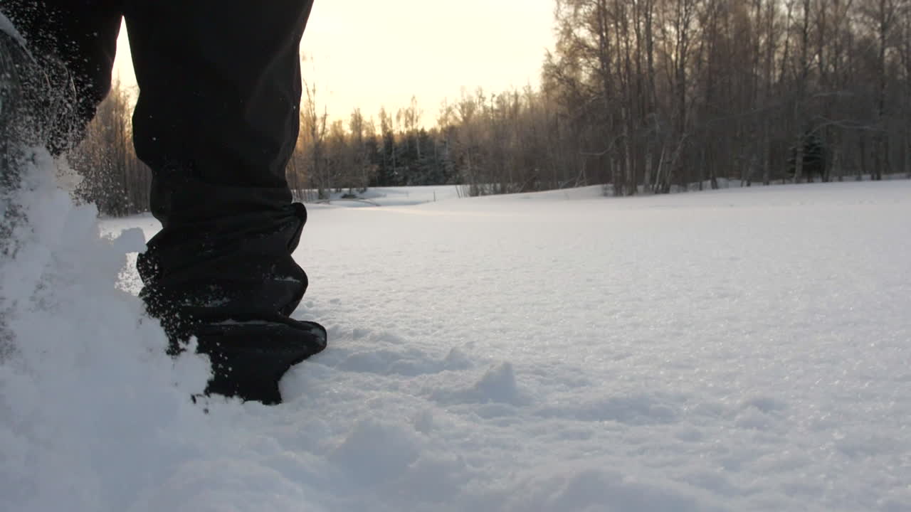 persona caminando a través de la nieve blanca pura y profunda en el área forestal, tiro de espalda de primer plano de ángulo bajo