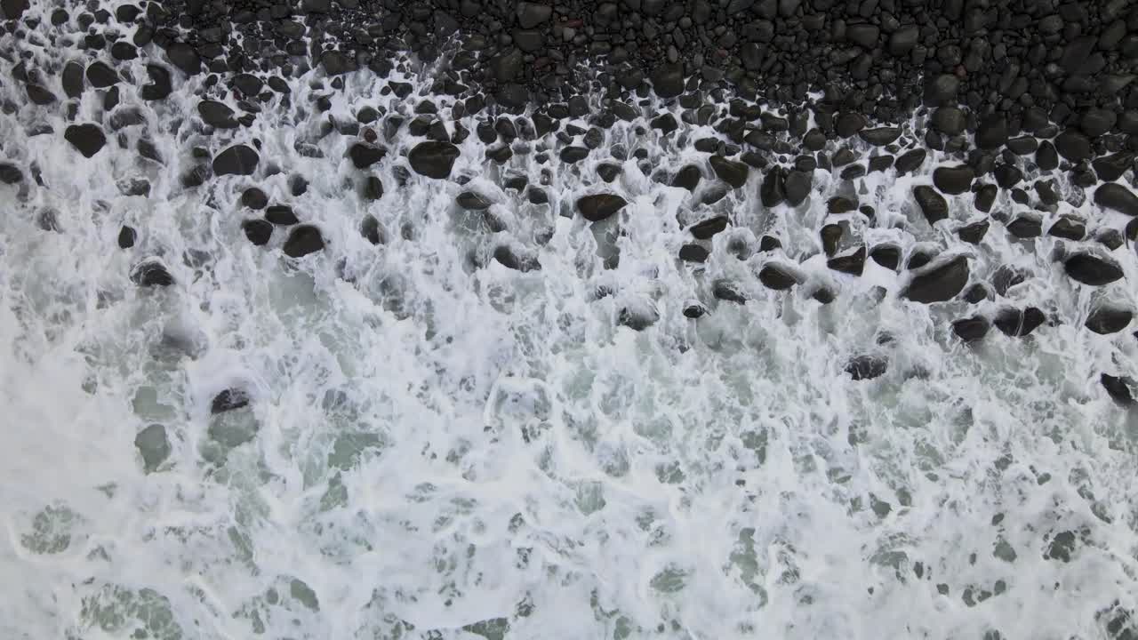 Static top-down drone view of a rugged, rocky beach on Hawaii's Big Island, featuring powerful, frothy white waves