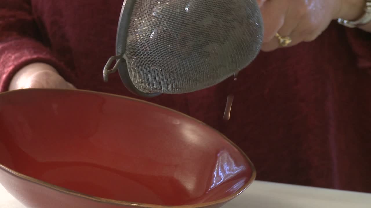 A woman pours olives from a strainer into a bowl