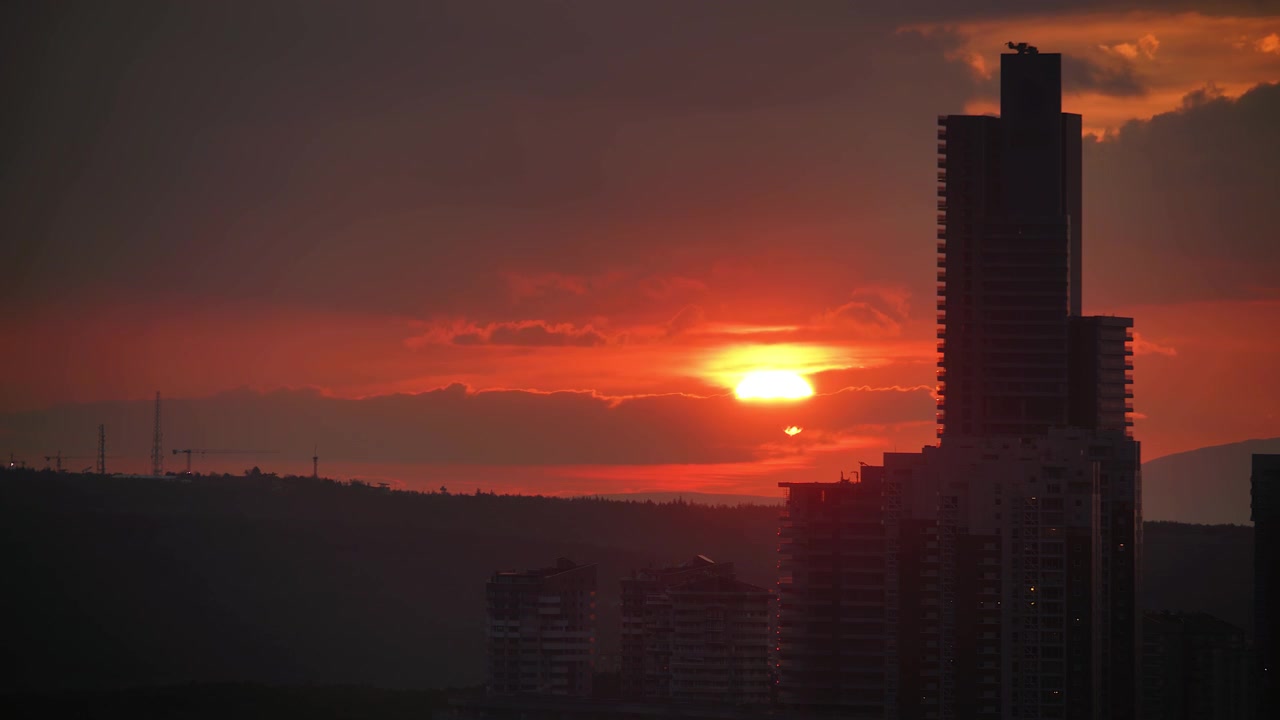 Pôr do sol sobre o horizonte de uma cidade moderna com edifícios em silhueta.
