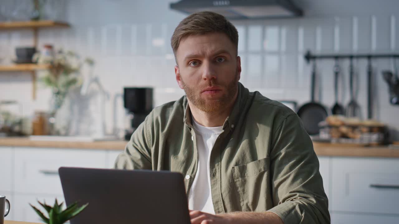 Smart student studying online by laptop at home kitchen closeup. Bearded man