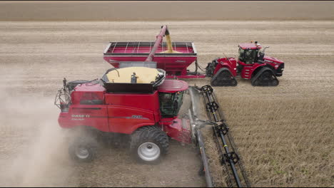 combine harvester collecting soybeans and transferring to moving grain cart in farm field, aerial