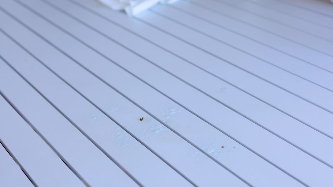 A gloved hand sprays and wipes a table, demonstrating effective cleaning techniques with bright lighting and close-up shots