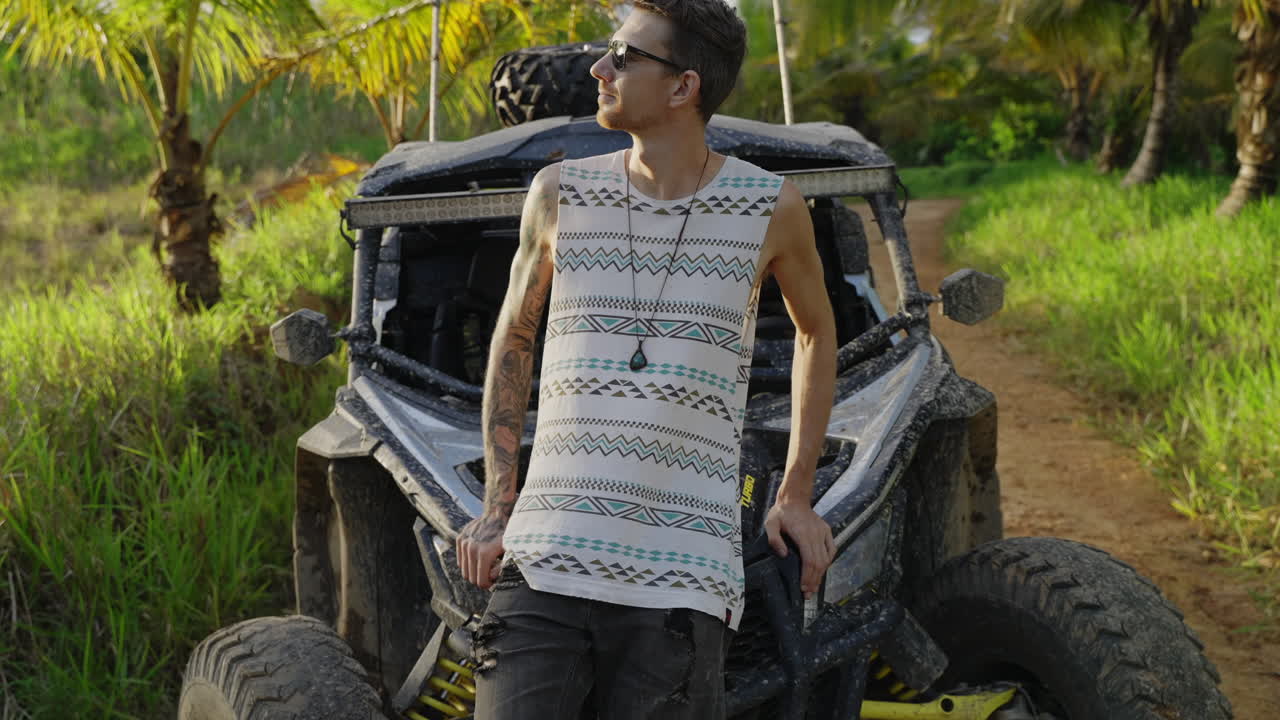 흙 버기와 접는 팔의 보닛에 기대어 선글라스를 착용하는 남성