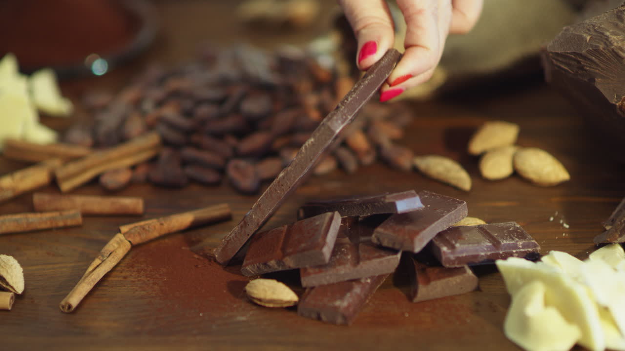 가까운 여성 손이 나무 테이블에 초콜릿 바를 놓고 있습니다.