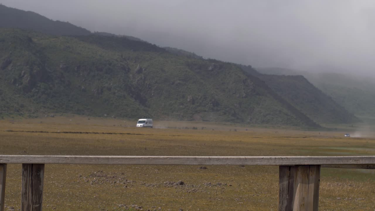 Beautiful woman hikes on windy day across wooden bridge as caravan car drives in distance