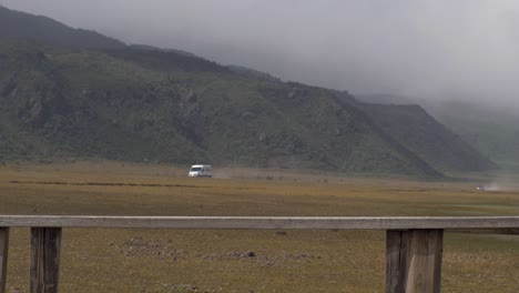 beautiful woman hikes on windy day across wooden bridge as caravan car drives in distance