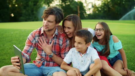 Parents-and-children-using-tablet-in-park.-Family-having-video-call-on-pad