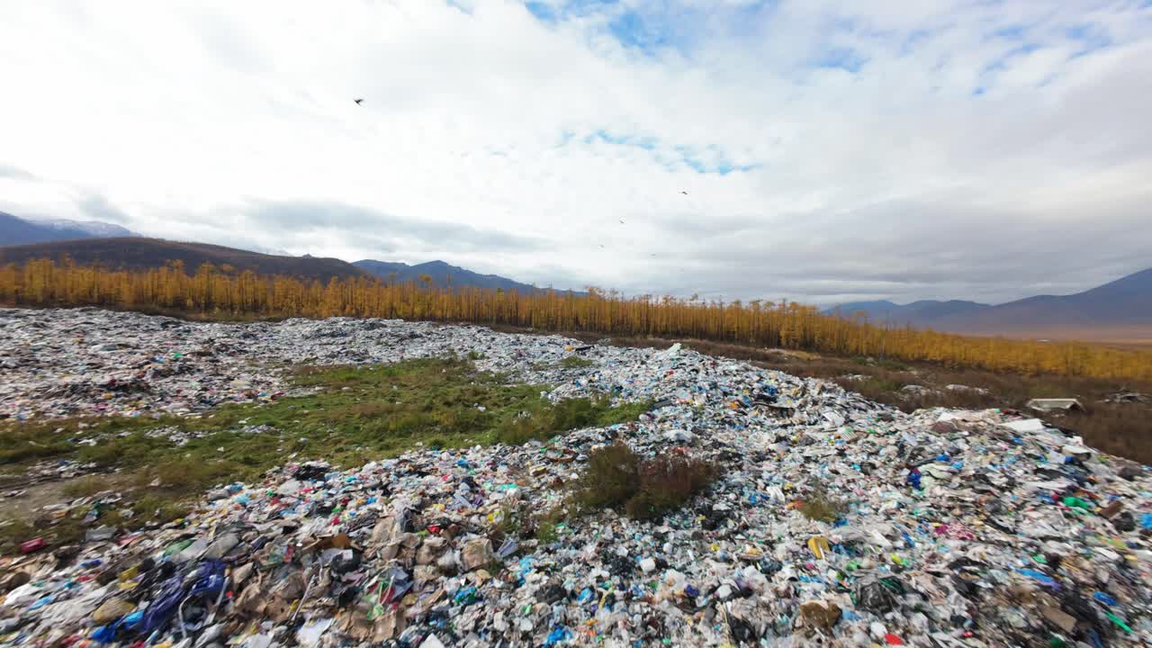 A vast expanse of discarded household items stretches across the landscape, surrounded by mountains and a dreary sky