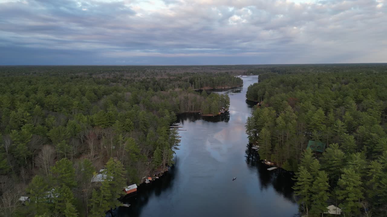 vista aérea de un piragüista remando en un río tranquilo, rodeado de denso bosque y cielos nublados