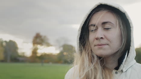 portrait of a young pensive woman in an autumn park. standing in a jacket with a hood on her head