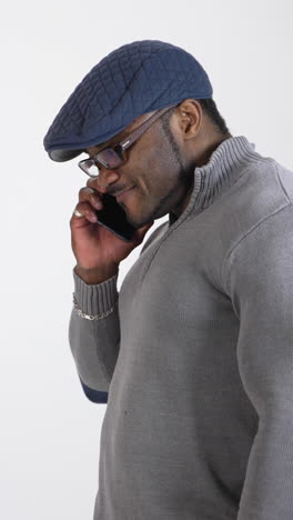 smiling black skinned man doing a phone call. happy young african man wearing glasses and cap talking the phone isolated on white in studio. vertical video