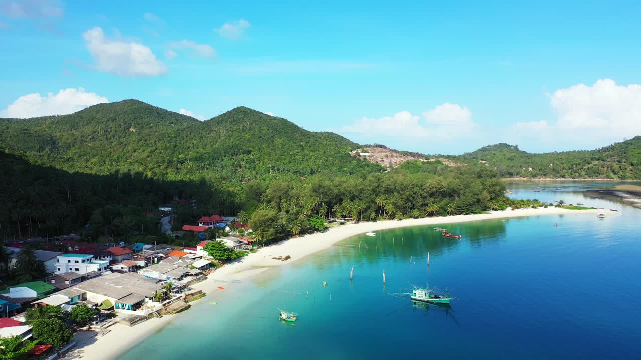 Barche da pesca ancorate sulla superficie calma e a specchio di una laguna blu turchese che riflette il cielo luminoso su una spiaggia di sabbia bianca di un'isola tropicale a Koh Pha Ngan, Thailandia.