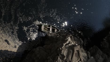 small wooden fishing boat floating on the water, anchored to the rocks with a rope