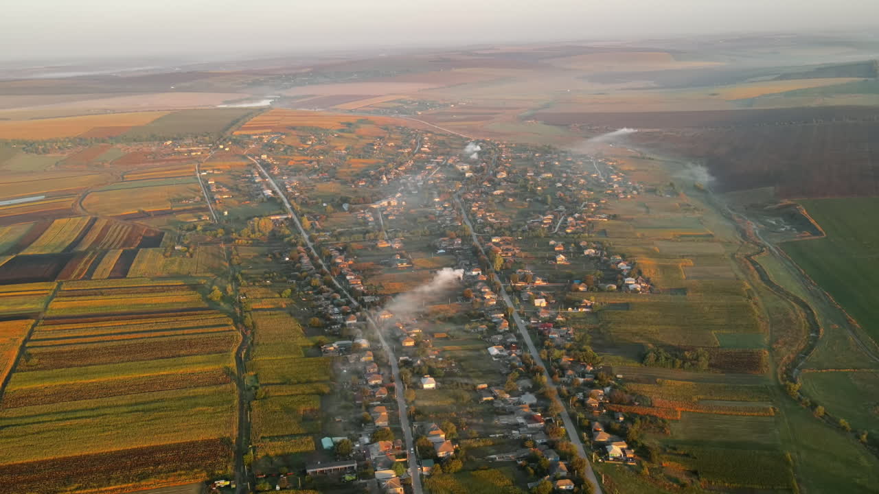 Aerial drone view of village in Moldova at sunset. Few columns of smoke from fires, wide fields
