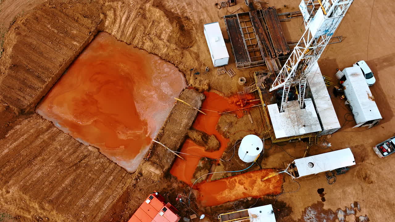 Descending over the site for production oil or gas. Tall derrick producing water flowing into the square pool.