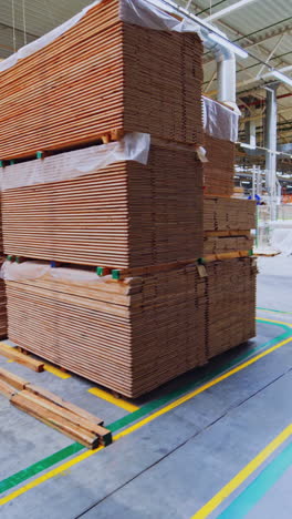 Large warehouse of timber materials. Motion camera inside the warehouse. Neatly stacked wooden boards for floor production in a warehouse. Vertical video