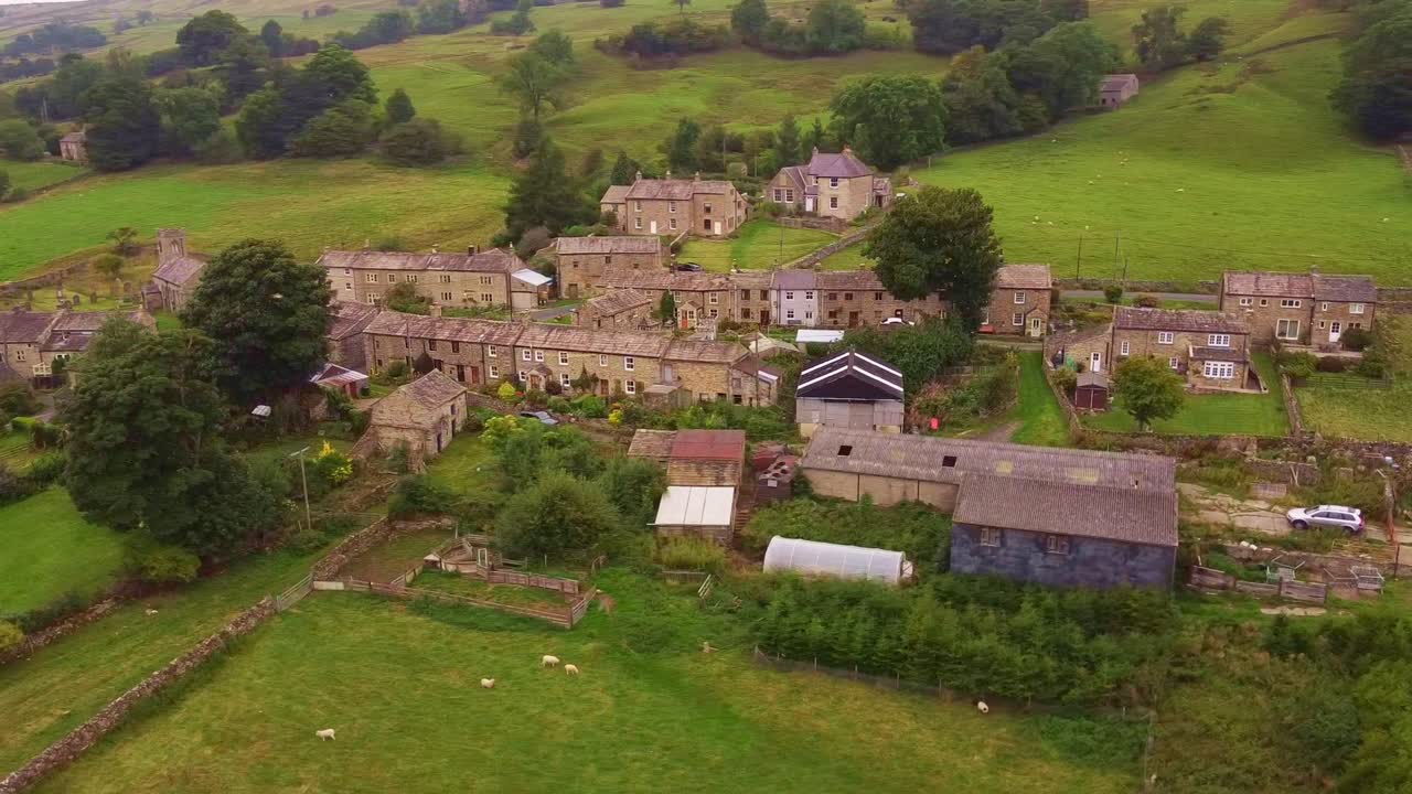Aerial shot rotating village in Yorkshire Dales valley with patchwork fields