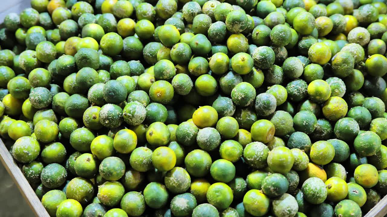 Tumpukan calamansi hijau dan kuning menunjukkan tekstur dan kesegaran di pasar