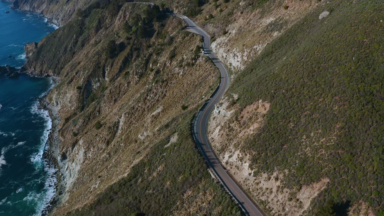 Aerial over coastline near a highway that runs through a mountain.