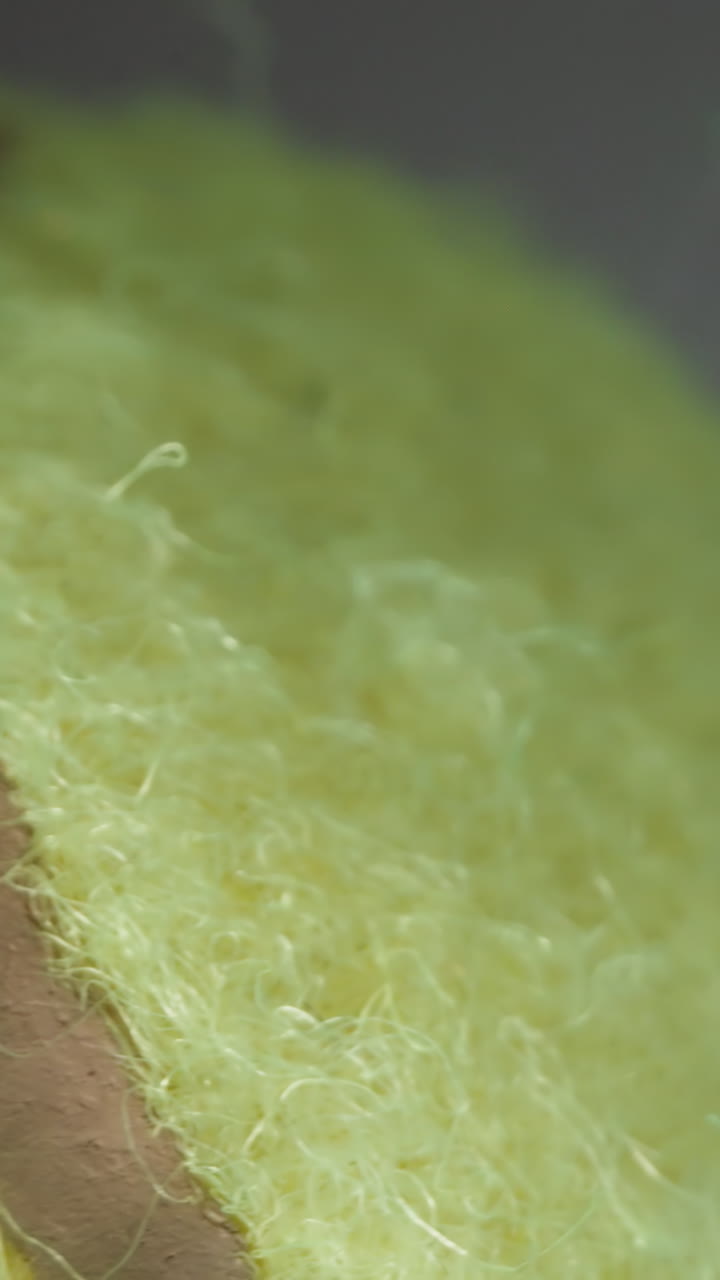 Fluorescent yellow tennis ball lies on table near window in dark apartment. Sphere covered with fiber felt for comfortable use in sports game on blurred background macro