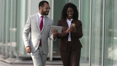 cheerful young managers walking on street with digital devices