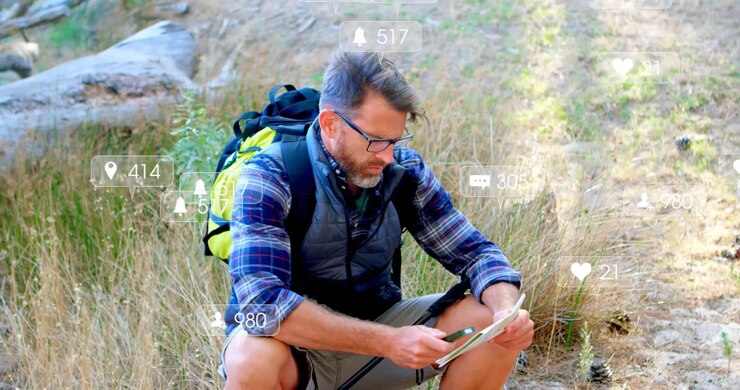 Hiker crouching on trail, tapping tablet with stylus checking route and causing social media alerts