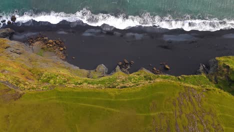 aerial rising shot of a steep cliff face on a black volcanic beach in iceland