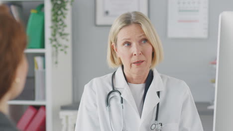 mature female doctor or consultant wearing white coat having meeting with female patient