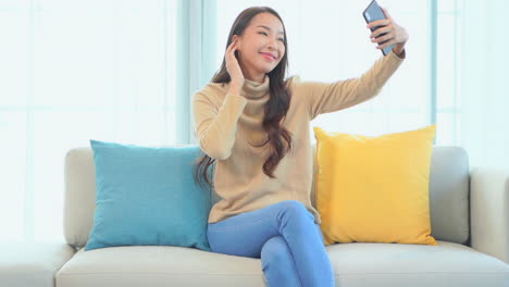 young asian woman taking selfie photo with smartphone in home interior, slow motion