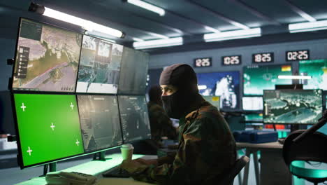 Special-forces-spy-examining-data-in-monitoring-room-with-chroma-key-monitors