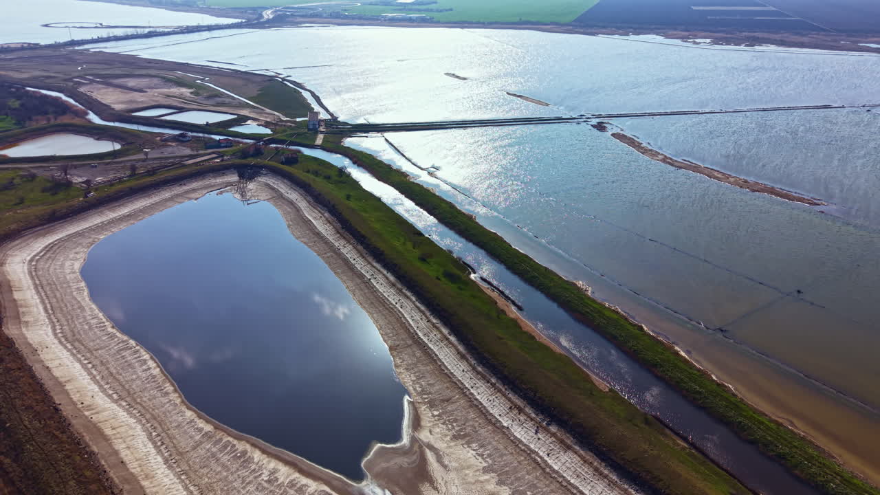 Vaste étendue d'eau dans un paysage plat avec des rives boueuses et des espaces verdoyants, révélant les diverses teintes de la nature à la lumière du jour.