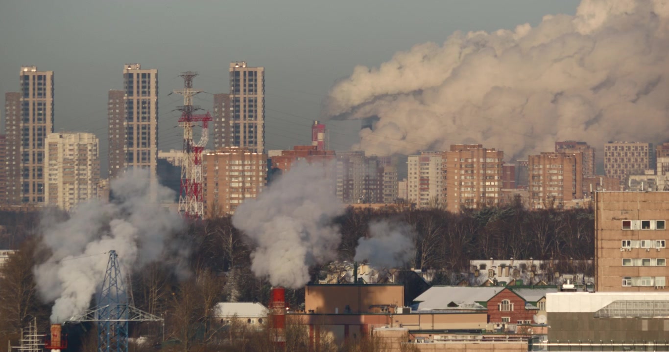Dense steam and smoke rise among snowy city buildings below tall residential towers for winter pollution district heating urban energy and environment themes