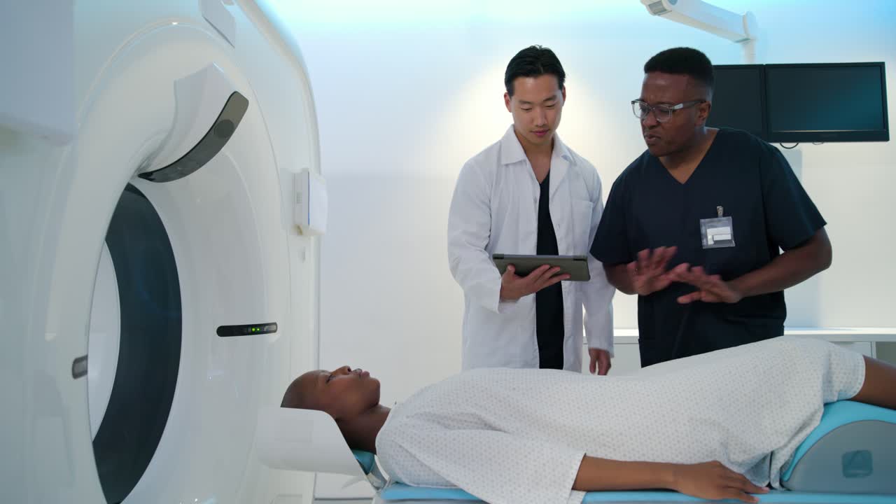 Asian doctor and tech reviewing tablet checking African American female patient's scanner alignment
