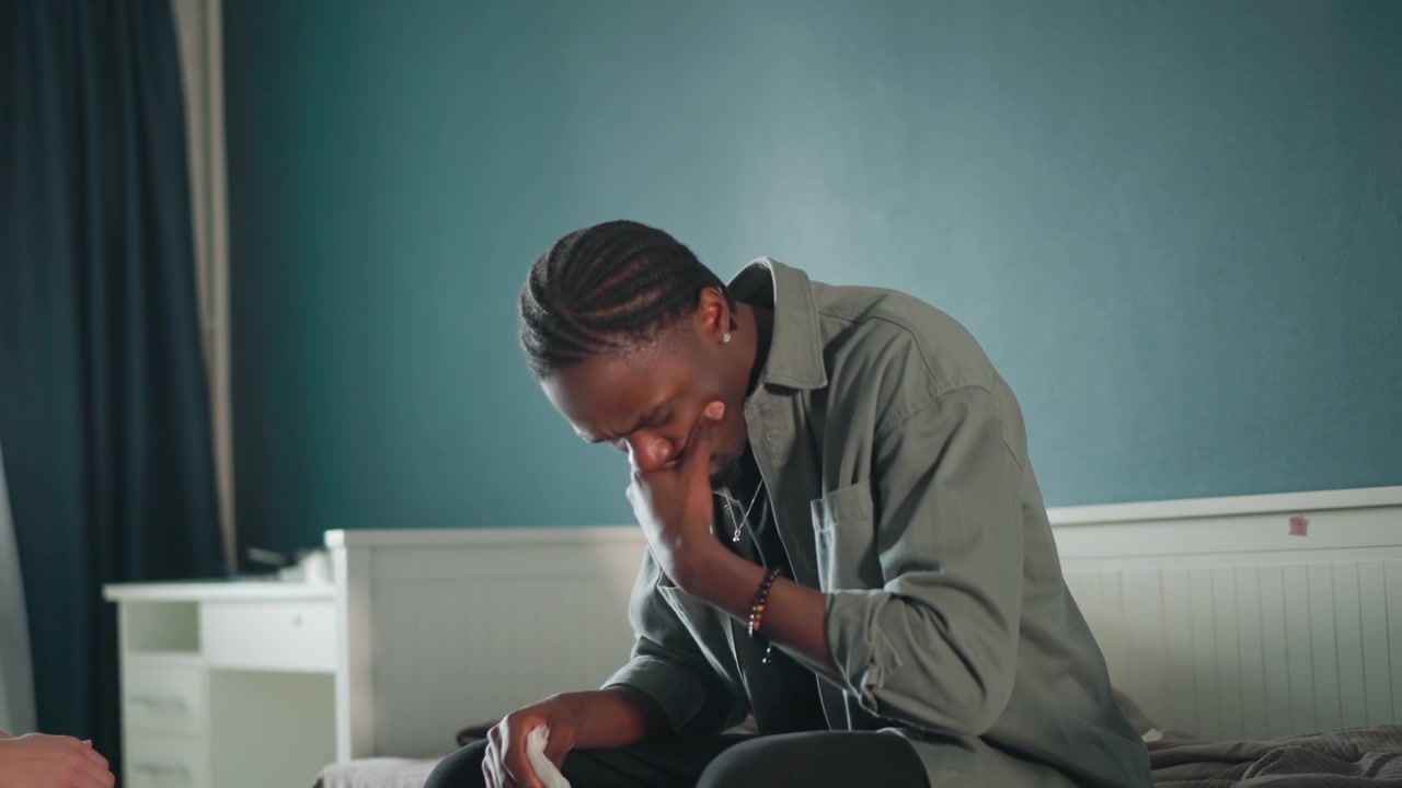 Tense man anticipates emergency. Emotionally distressed man anxiously waits for paramedic response. Man seated on bed shows anxiety as he waits for emergency responders in dimly lit room