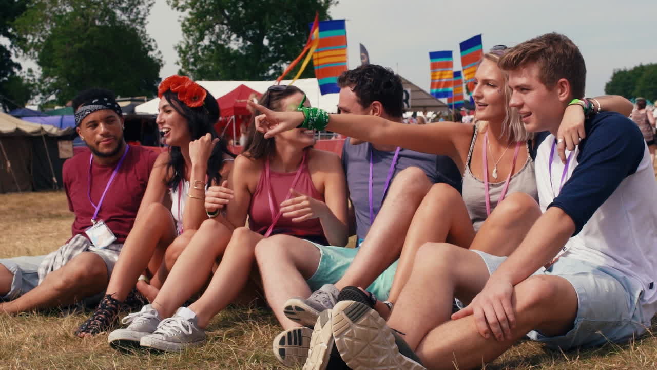 친구 들 이 잔디 에 앉아 음악 축제 에서 공연 을 보고 있다