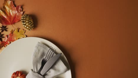 video de un plato con cubiertos y decoración de otoño con hojas en superficie naranja