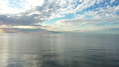 Antenne:-Während-Der-Goldenen-Stunde-Sehr-Langsam-über-Dem-Meer-Fliegen,-Mit-Majestätischem-Horizont-Und-Blauen-Farben-Am-Himmel