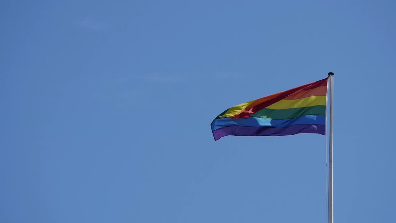 Waving rainbow flag for gay community on a long flagpole. Clear blue sky. LGBT symbolism and activisim during pride week. Minorities rights.