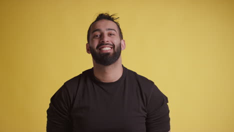 head and shoulders studio portrait of smiling young man against yellow background