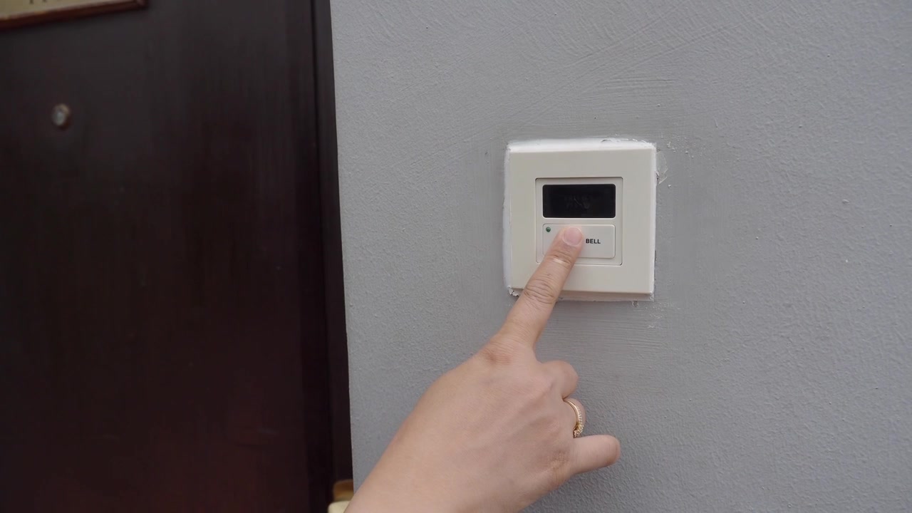 Persona che preme il pulsante del campanello sul muro