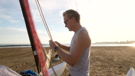 man tying knots while preparing a sailing cat on the beach