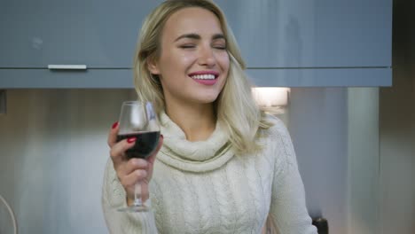 Cheerful-woman-drinking-wine-in-kitchen