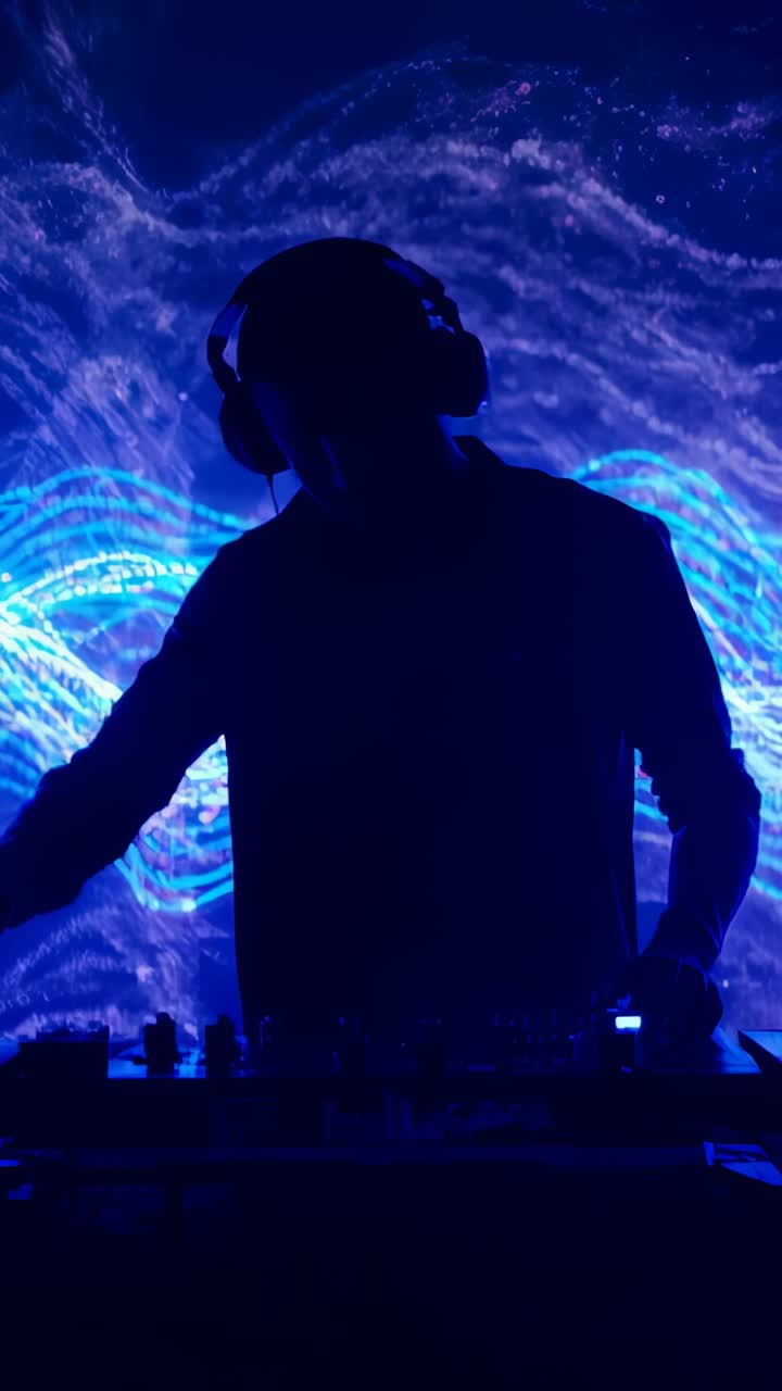 Vertical video: Reacting to waves, backlit DJ with headphones mixing on stage with mixer, jog wheel