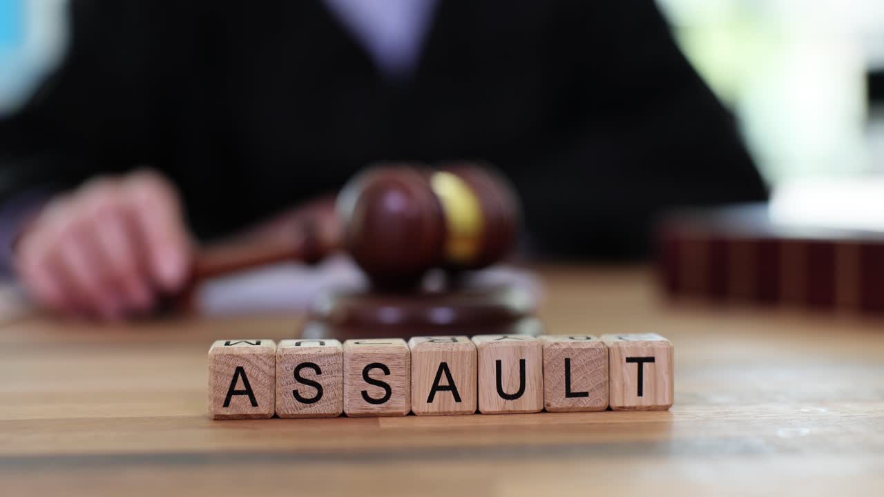 The word "Assault" spelled out in wooden blocks with a judge holding a gavel in the background