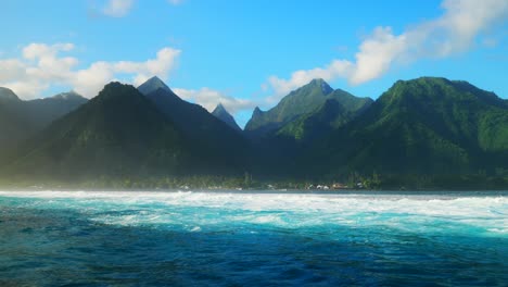 towering mountain peaks surfing surf calm waves teahupoo tahiti french polynesia crashing swell on shallow coral reef south pacific island  ocean waterhousing landscape blue sky super slow motion