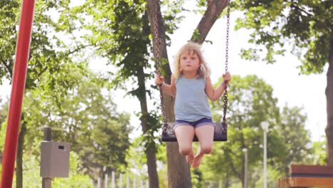 A-little-girl-swinging-in-the-park,-slow-motion,-hot-summer-day,-low-angle